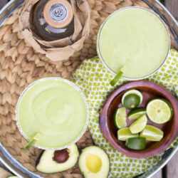 Two Avocado Margaritas with lime wedges on a tray.