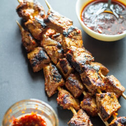 Malaysian satay skewers beside an open jar of chili sambal.