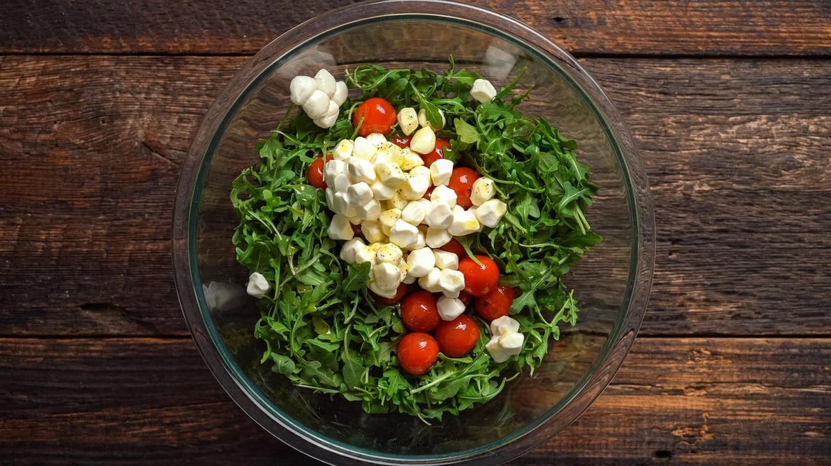 A glass bowl with a fresh arugula salad topped with cherry tomatoes and mozzarella balls.