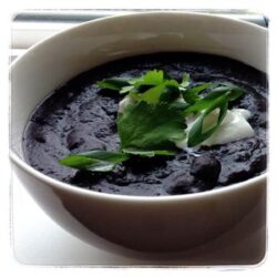 A bowl of creamy black bean soup, garnished with fresh cilantro and a dollop of sour cream.