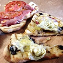 Two grilled pizzas on a wooden board.