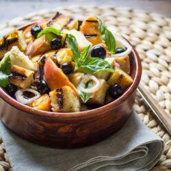 A bowl of grilled Panzanella salad with peaches, blueberries, grilled bread cubes, fresh basil, and shallots.
