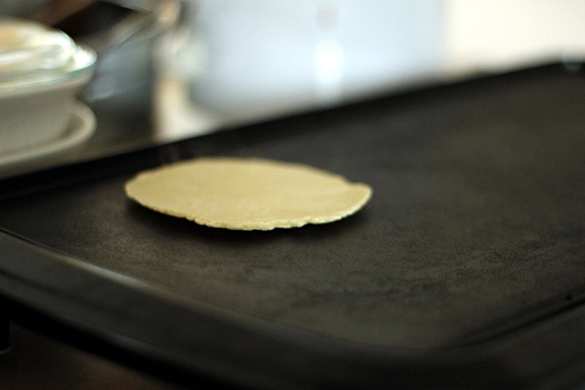 Cooking the homemade corn tortillas until they turn brown and the edges start to curve away from the griddle.