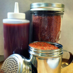 A squeeze bottle of Kansas City BBQ sauce with jars of rib rub and spices.