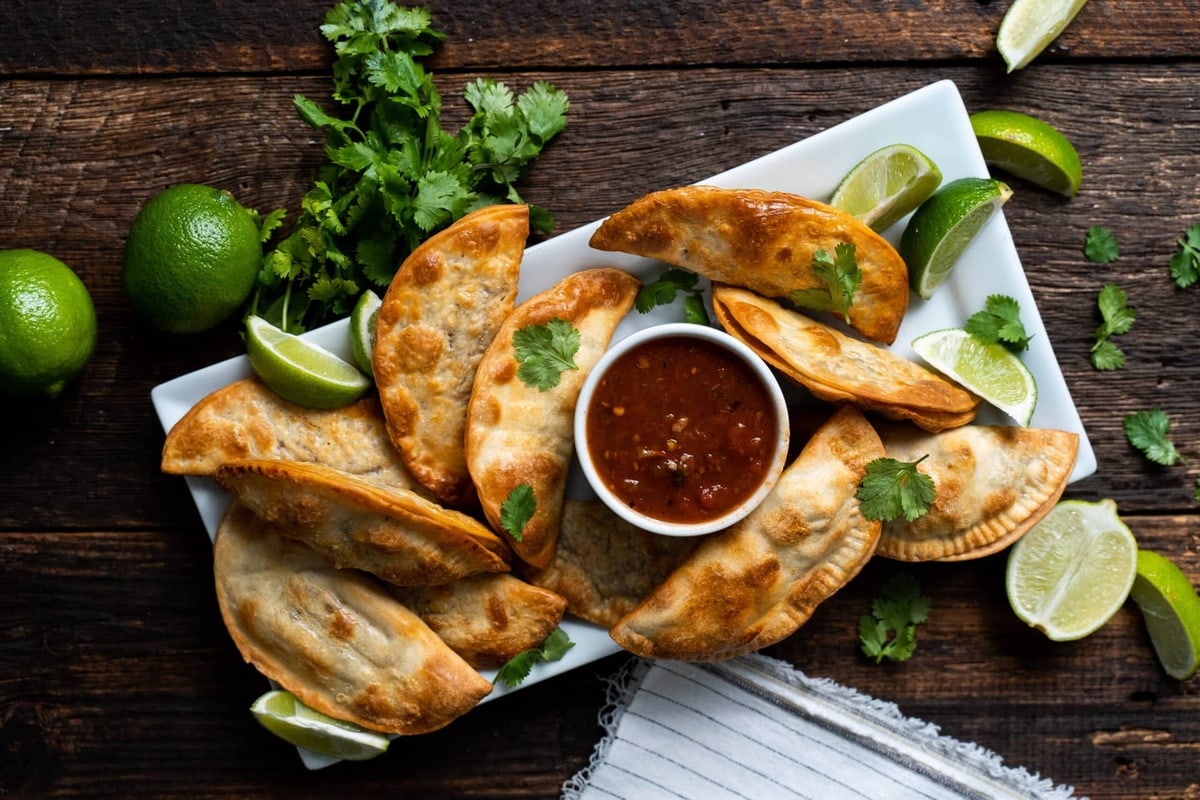 Puerto Rican empanadas on a white plate with a bowl of salsa.