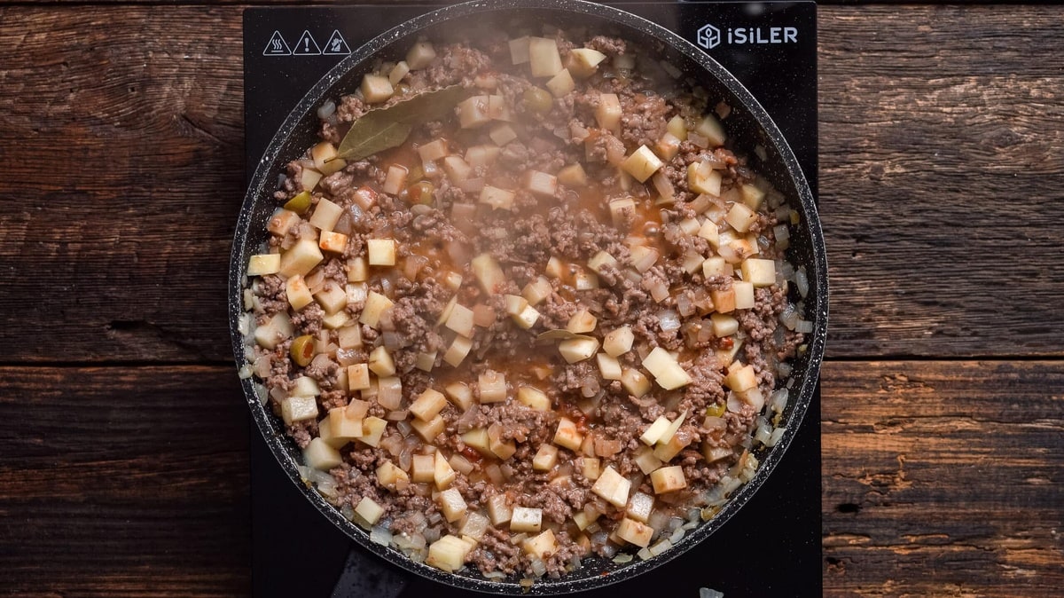 Puerto Rican picadillo simmering in a skillet with bay leaves.