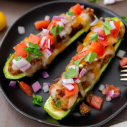 Zucchini boats filled with taco beef, tomatoes, and cilantro on a black plate.